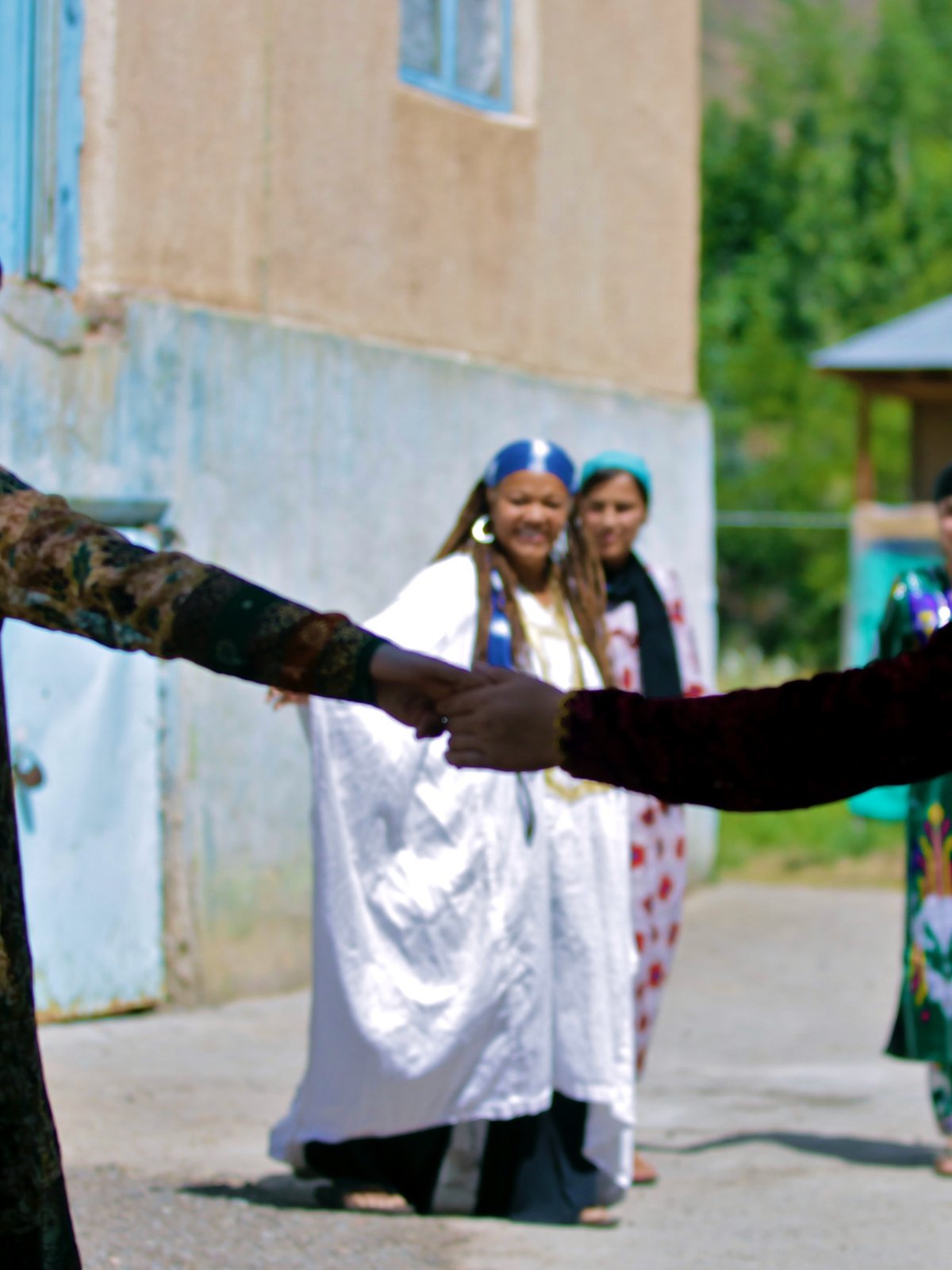 Amikaeyla in white at the center of a sunlit village hand-circle