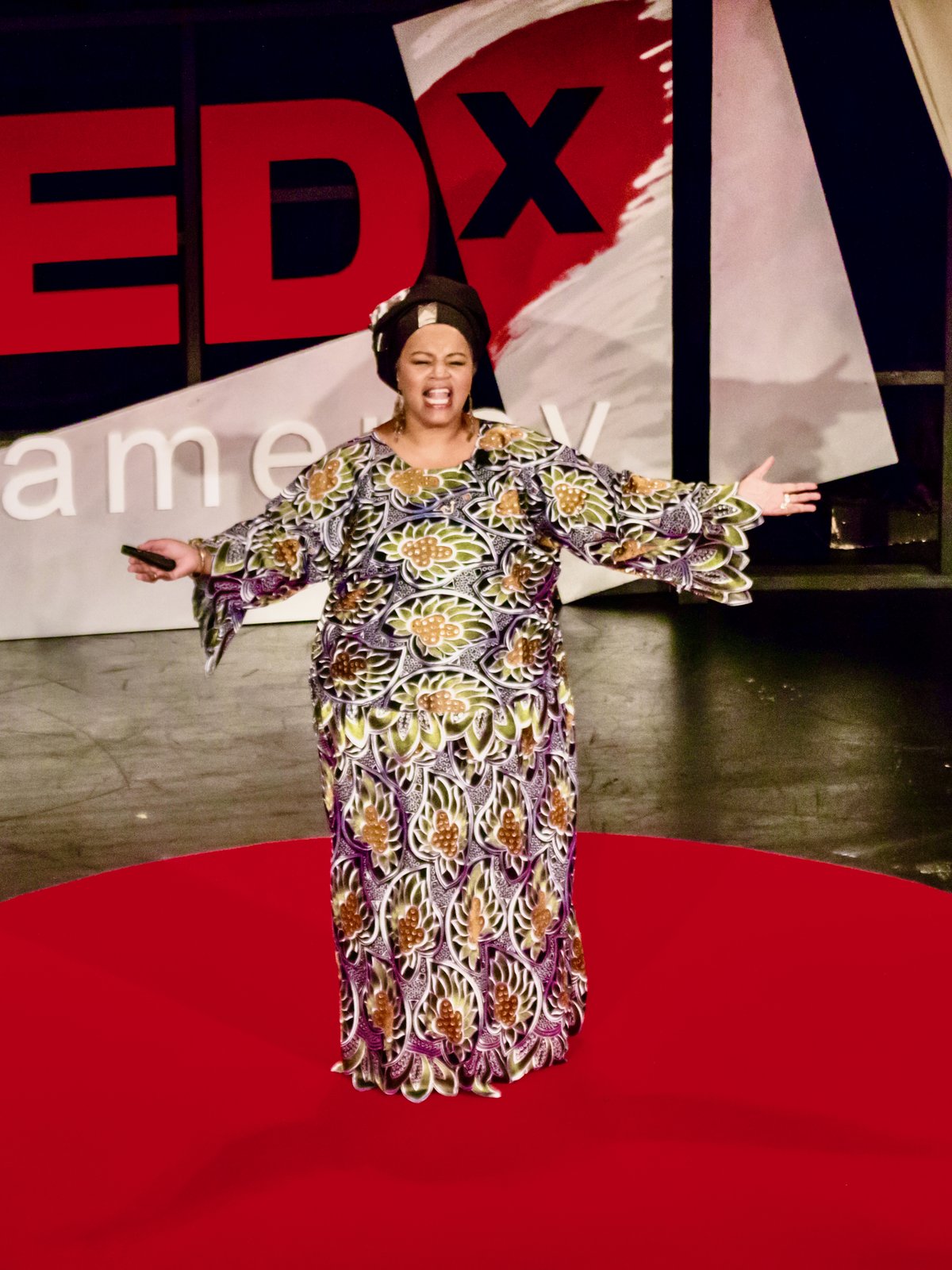 Amikaeyla on the TEDx Gramercy stage, arms wide on the red dot